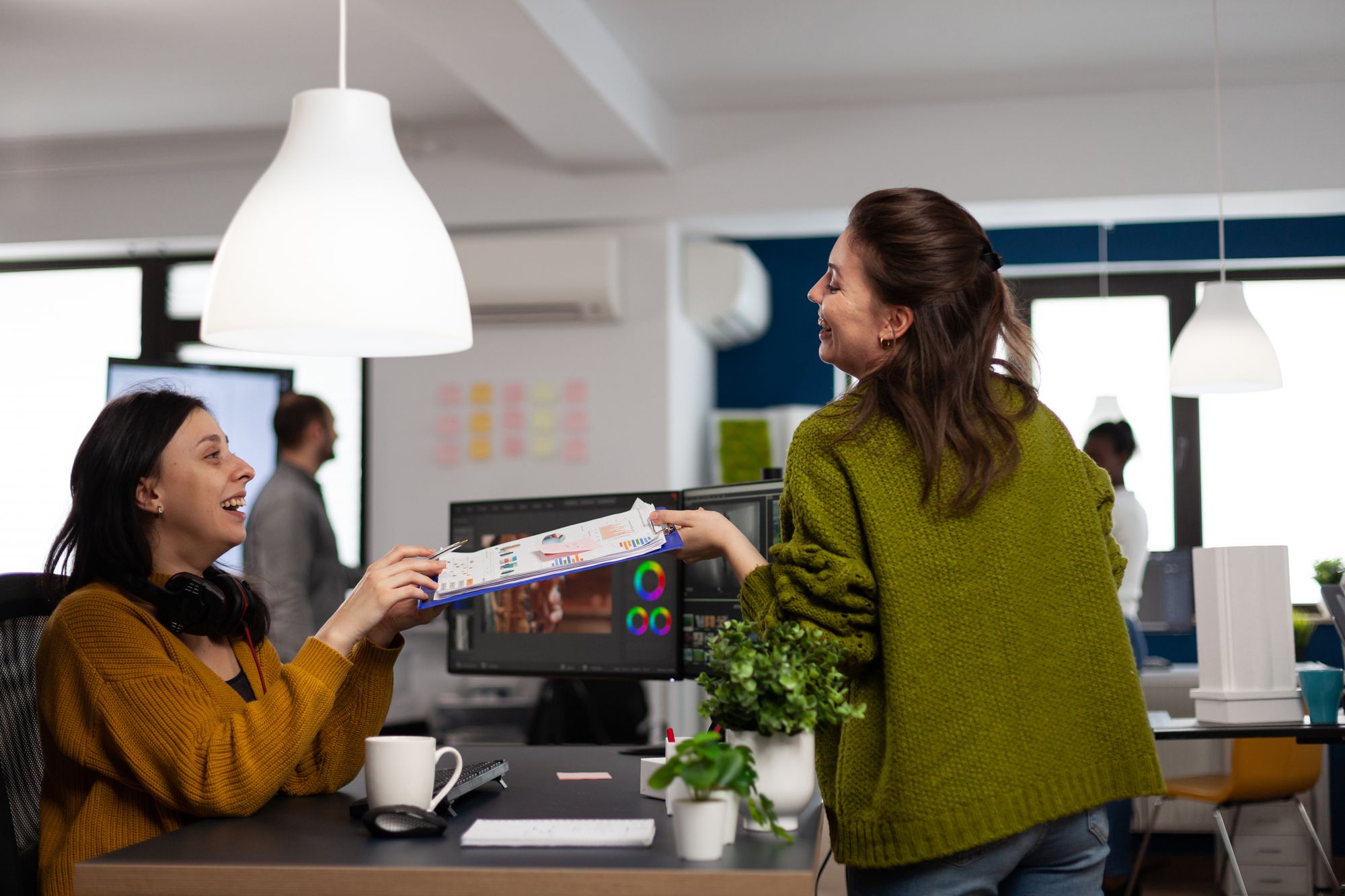 Happy coworkers talking about creative film montage looking at movie production ideas working in start up office with two monitors.